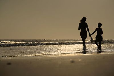 Women walking on beach against clear sky
