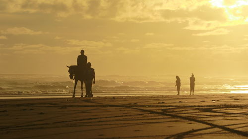 Silhouette men standing on beach against sky during sunset