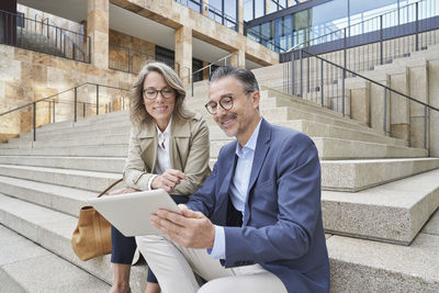 Mature business people using tablet pc sitting on steps