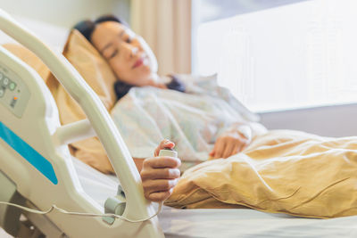 Woman patient holding emergency call button while lying in hospital bed
