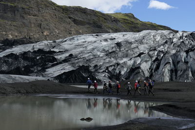 People walking by lake and rock formation