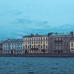 Buildings at waterfront against cloudy sky