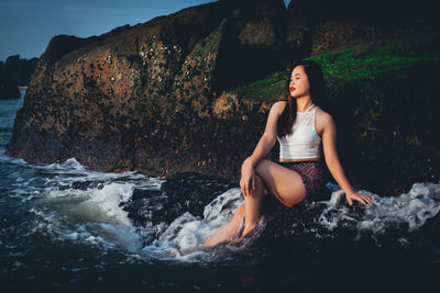 Young woman sitting on rock by sea