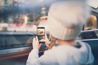 Rear view of girl photographing with mobile phone in bus