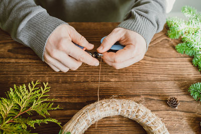 A man makes a christmas decoration for his home from fresh spruce branches and dried orange slices.