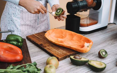 Young woman preparing organic juice with cold pressed extractor machine - focus on hand holding kiwi