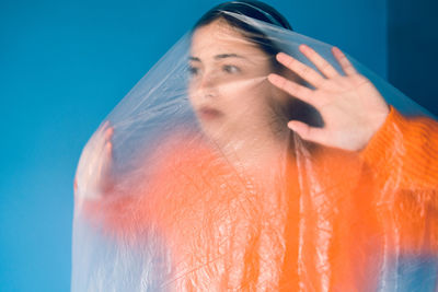 Teenage girl wrapped in plastic against blue background