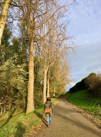 Rear view of woman on road amidst trees against sky