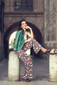 Portrait of smiling young woman sitting on bollard