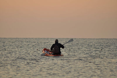 Rear view of man in sea against sky during sunset