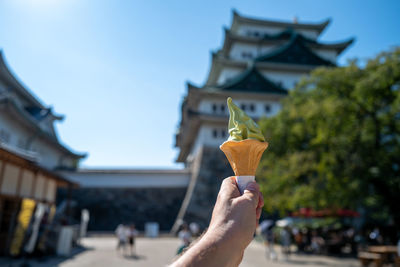 Cropped hand of man holding ice cream against building