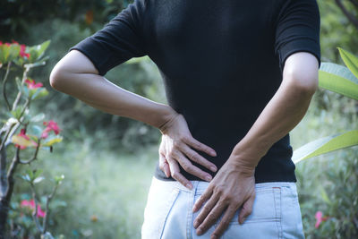 Rear view of woman touching back in pain while standing by plants