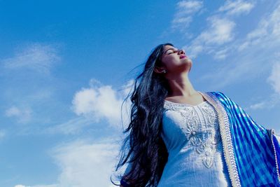 Low angle view of woman standing against blue sky