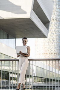 Female business professional using laptop while leaning on railing