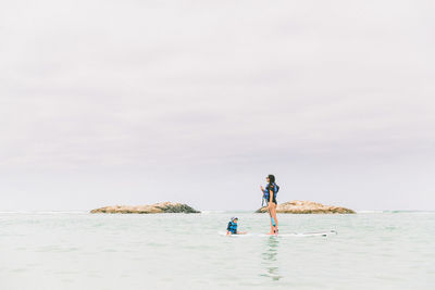 Woman with baby boy on paddleboard in sea against sky