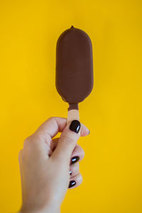 Cropped image of woman holding ice cream bar on yellow background