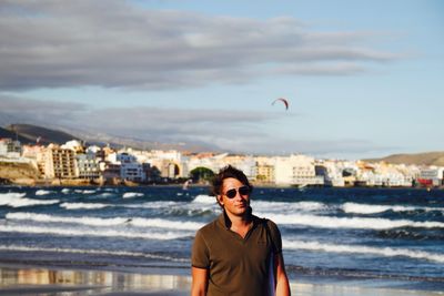 Young man wearing sunglasses at beach against sky