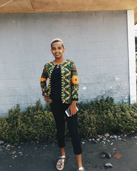 Portrait of a smiling young woman standing against wall