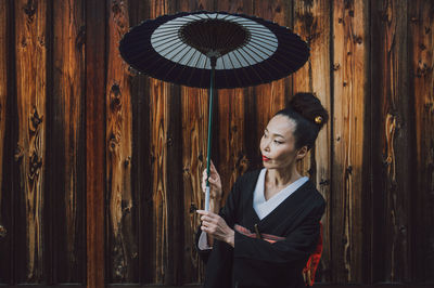 Woman holding umbrella standing against wooden wall