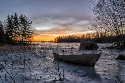 Boat moored in winter against sky during sunset