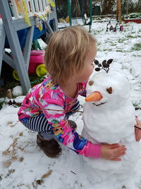 Cute girl playing with snowman during winter