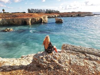 Rear view of woman on rock by sea against sky