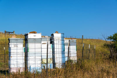 Beehives on grassy field against clear blue sky