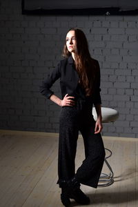 Portrait of young woman standing against brick wall