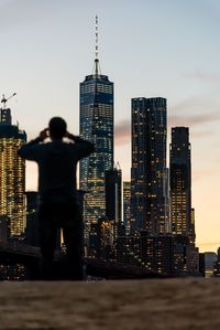 Rear view of man against brooklyn bridge and one world trade center in city