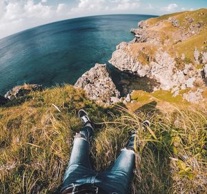 Low section of man on cliff by sea against sky