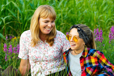 Mother and daughter sitting on meadow and smiling. friendship love concept. woman and girl 