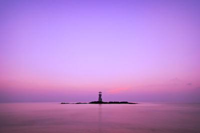 Silhouette lighthouse by sea against sky during sunset