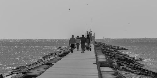 People walking on pier over sea against clear sky