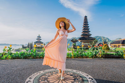 Woman standing at pura ulu danau temple against sky during sunrise