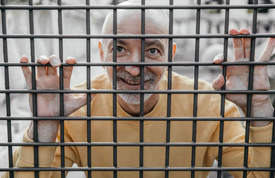 A playful expression captures the elderly man looking through metal bars