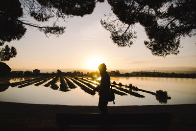 Silhouette man standing by lake during sunset