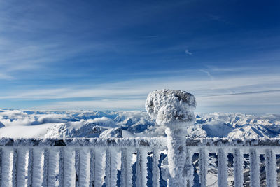 Icicles on wooden post against snowcapped mountains against blue sky