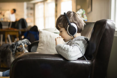 Side view of boy eating food while sitting on armchair at home