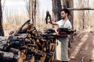 Side view of male in apron taking logs from pile of firewood in forest for picnic