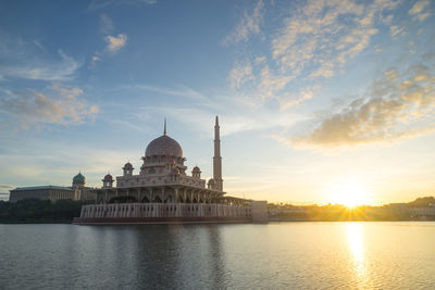 Mosque by river against sky during sunrise