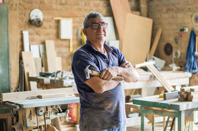 Elderly carpenter posing with crossed arms in his workshop