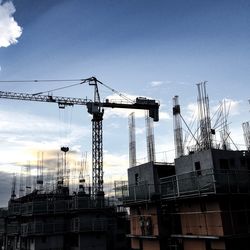 Low angle view of cranes against sky in city