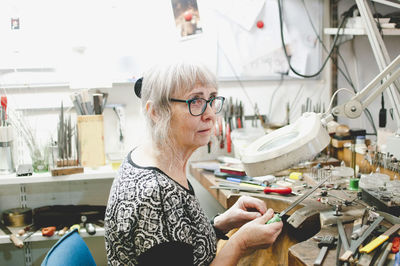 Senior craftsperson looking away while making jewelry in workshop