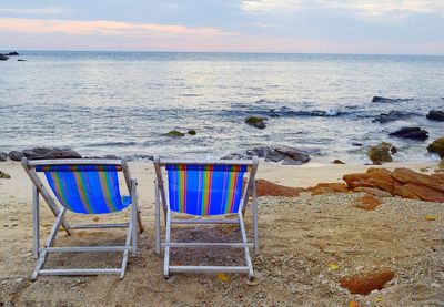 Chairs on beach against sky during sunset