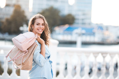Portrait of smiling woman holding bag standing outdoors