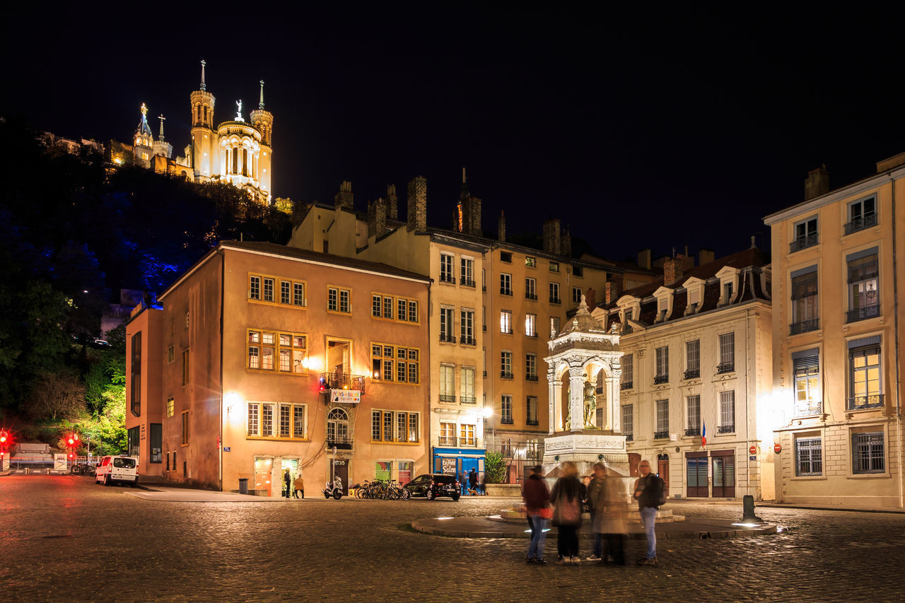 PEOPLE ON STREET BY ILLUMINATED BUILDINGS IN CITY AT NIGHT