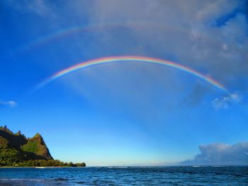 Scenic view of rainbow over sea against blue sky