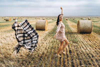 Smiling woman in sunglasses with bare shoulders on a background of wheat field and bales of hay.