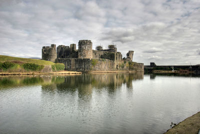 Caerphilly castle by lake against cloudy sky