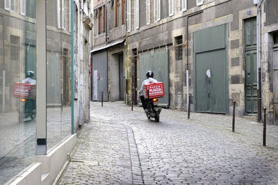 Rear view of man walking on street amidst buildings in city